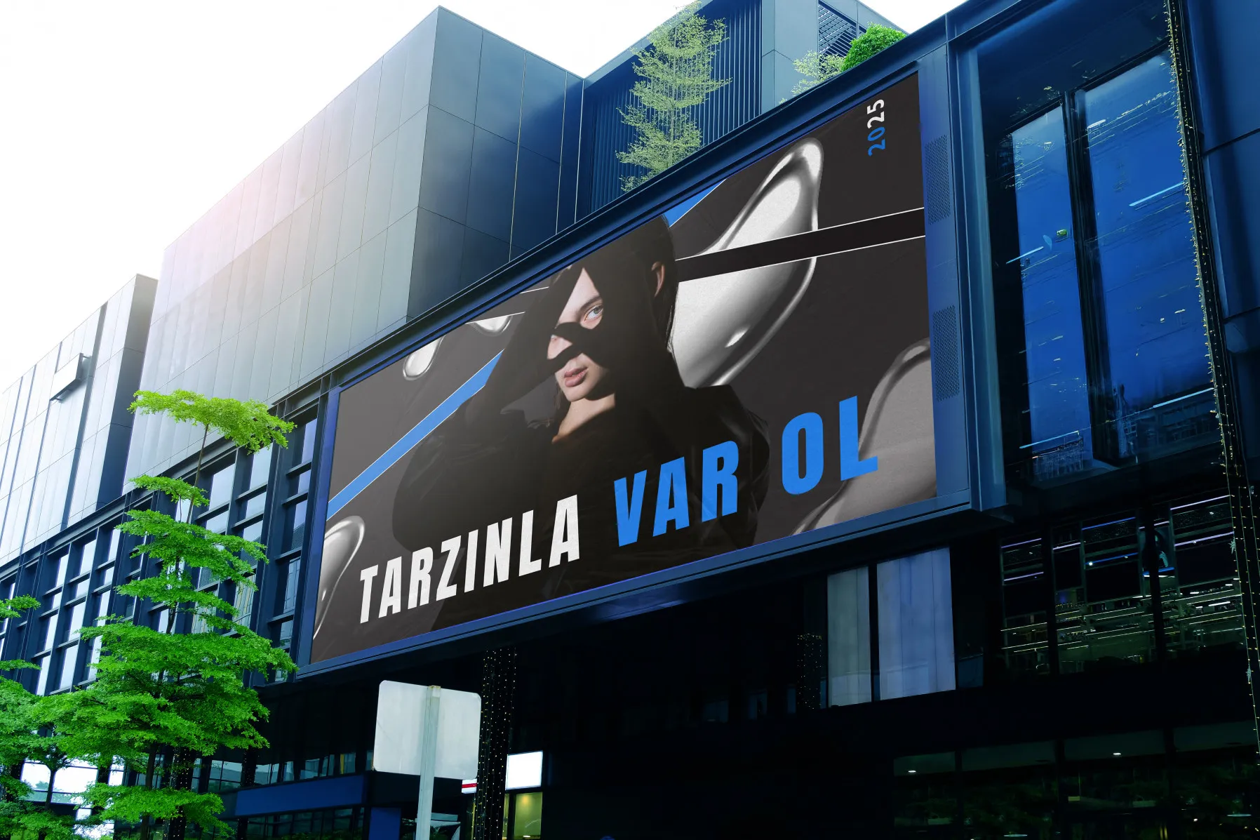 Modern bir binanın üzerindeki büyük bir açık hava reklam panosunda elini yüzüne götürerek poz veren bir kişi görülüyor. Türkçe metinde kalın beyaz ve mavi harflerle TARZINLA VAR OL yazmaktadır.