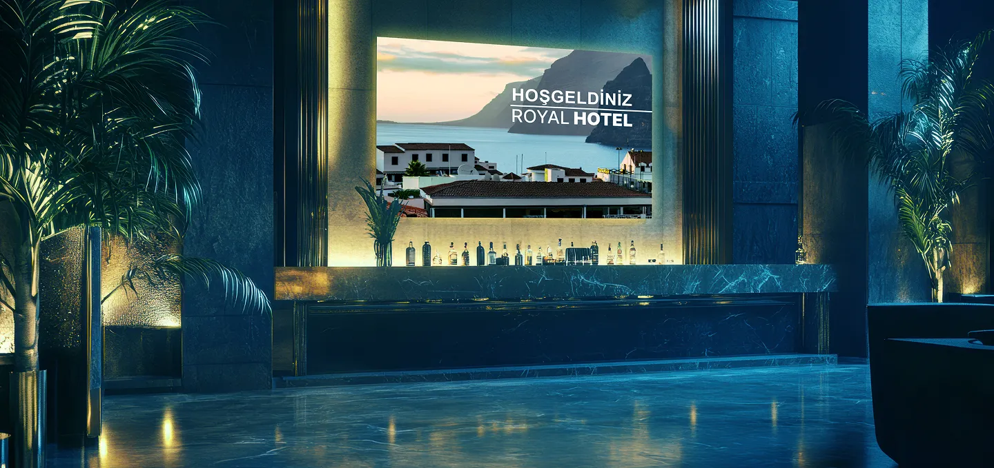 Koyu mermer zeminli modern bir otel lobisi, yemyeşil saksı bitkileri ve resepsiyon masasının arkasında dağların ve binaların doğal bir fotoğrafının üzerinde HOŞGELDİNİZ ROYAL HOTEL yazan büyük bir ışıklı tabela.