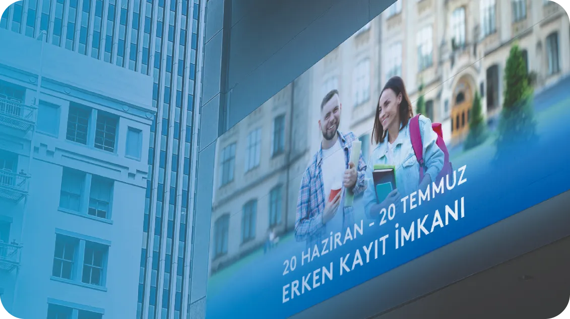 Bir şehir binasının üzerindeki dijital reklam panosunda, ellerinde kitap tutan iki gülümseyen öğrenci görülüyor. Türkçe metin şu şekildedir: 20 Haziran - 20 Temmuz Erken Kayıt İmkanı, yani Erken Kayıt Fırsatı, 20 Haziran - 20 Temmuz.